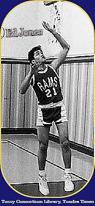 Black and white photo from the Tuzzy Consortium Library, the Tundra Times, showing Ed Jones in dark RAMS uniform, #21, under basket, up in air, having made his shot, in practice.Played for Kaveolook (Kavtovik) High School, Alaska.