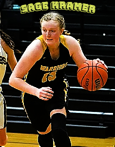 mage of Oregon girls basketball player, Sage Kramer, Philomath High School, shown driving with ball, in her black WARRIORS #15 jersey with yellow lettering.