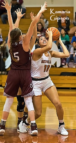 Image of Kamaria Gipson, Texas girls basketball player, 2018-19, for Beeville High School, in white #11 uniform, under basket, trying to go up for shot against two defenders.