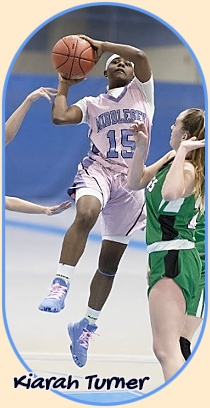Image of Kiarah Turner, Middlesex County ollege girls basketball player in 2020. Shown coming towards us, up in the air with a layup, in her blue on white #15 uniform, guarded by two on defense.
