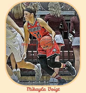 Photo of Mikayla Voigt, Northern Illinois University women's basketball player in game action, in red HUSKIES unifor, #21 bringing basketball upcourt towads our left.